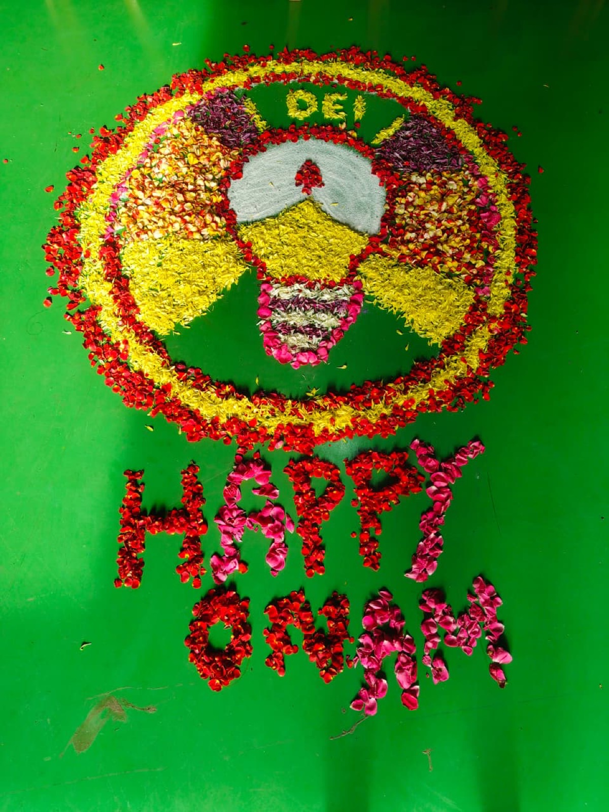 Floral pookalam featuring the DEI bulb emblem and a Happy Onam greeting